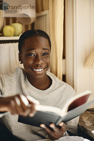 Portrait of smiling boy holding book while sitting at home