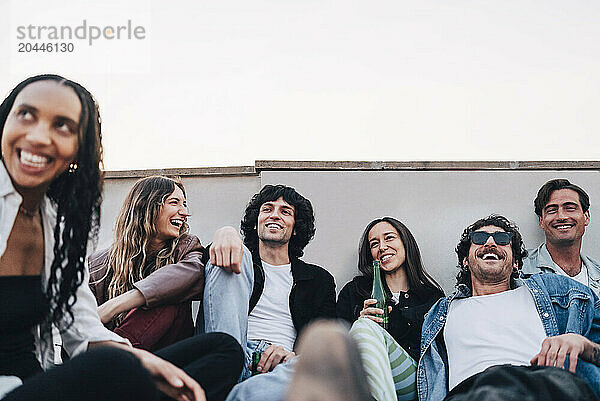 Low angle view of smiling male and female friends enjoying drinks at rooftop party