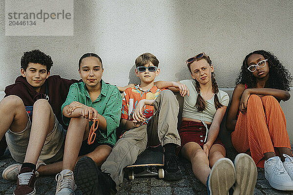 Group of cool friends sitting on ground against wall