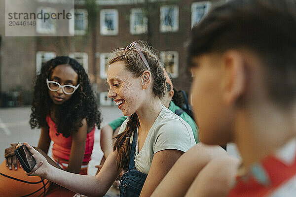 Happy girl using smart phone with friends at school campus