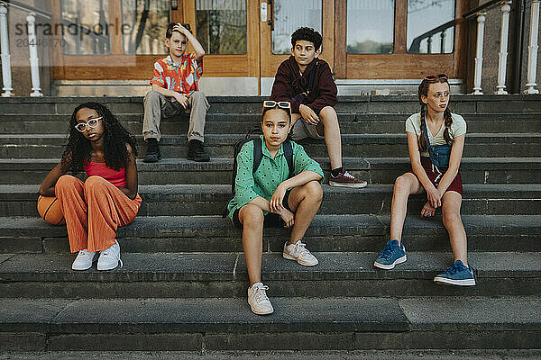 Portrait of girl sitting with friends on staircase in front of school building entrance