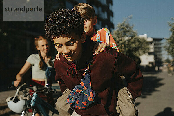 Boy piggybacking friend while walking at street