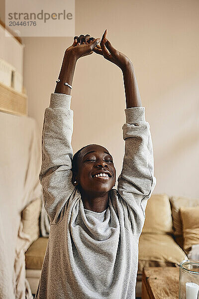 Smiling teenage boy stretching arms while doing yoga at home