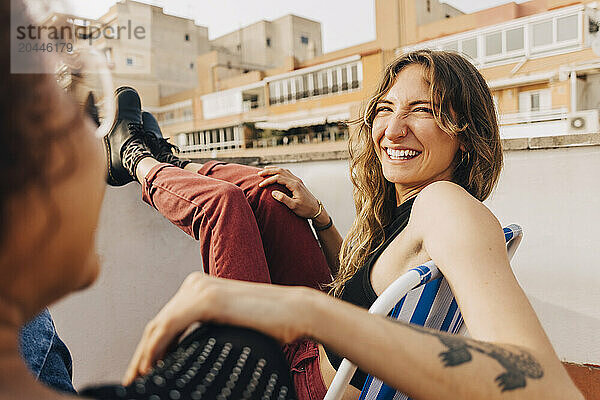 Smiling young woman talking with female friend sitting on rooftop