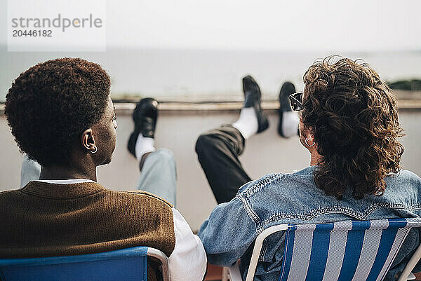 Rear view of male friends sitting on chairs on building rooftop