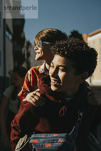 Happy boy piggybacking friend while walking at street