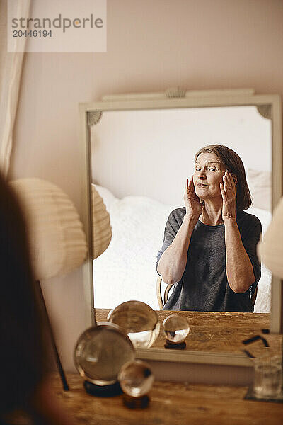 Senior woman taking care of skin looking in mirror at home