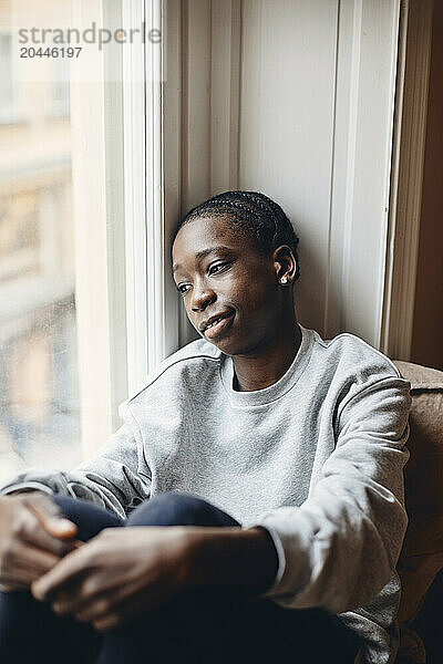 Tired teenage boy looking through window at home