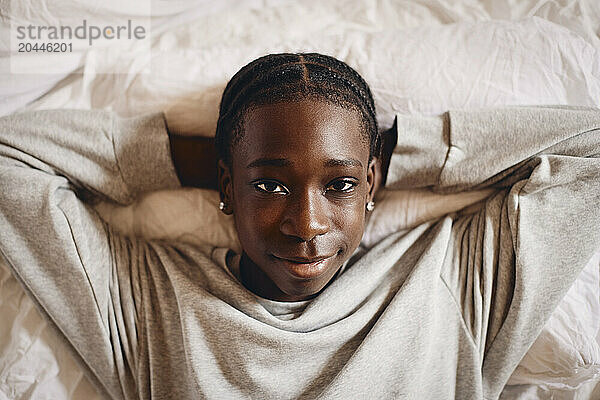 Portrait of teenage boy lying down with hands behind head on bed at home