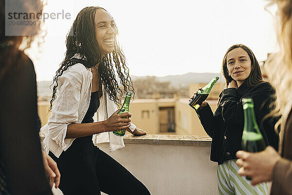 Happy female friends enjoying beer in party on building rooftop