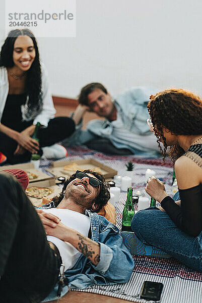 Group of male and female friends enjoying food and drinks at rooftop party