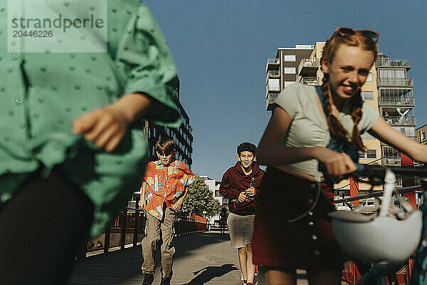 Male friends running on street while female friend walking with bicycle on street