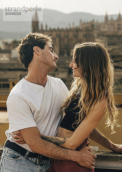 Romantic couple looking at each other standing near wall on rooftop