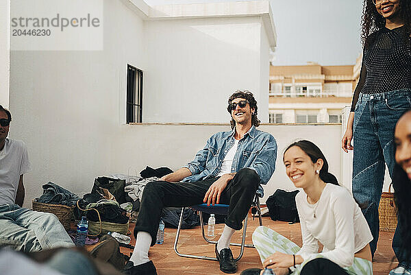 Smiling man sitting with male and female friends in party at rooftop