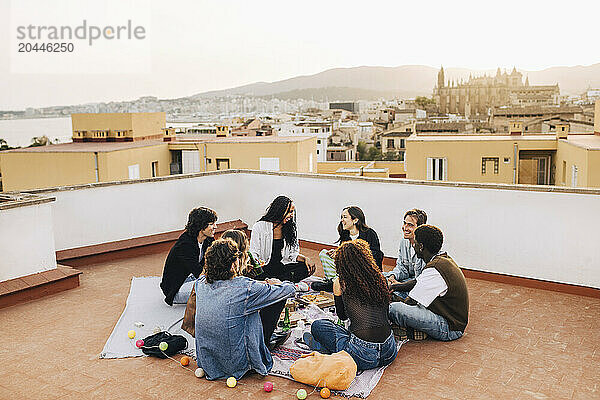 Male and female friends having food and drinks while sitting on building rooftop