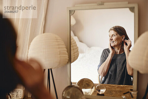 Smiling senior woman looking at reflection in mirror at home