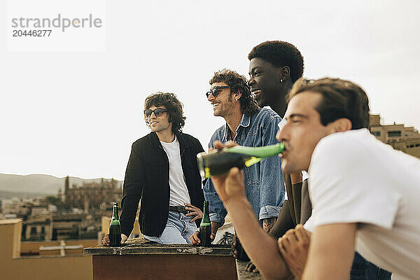 Multiracial male friends having beer during party on building rooftop