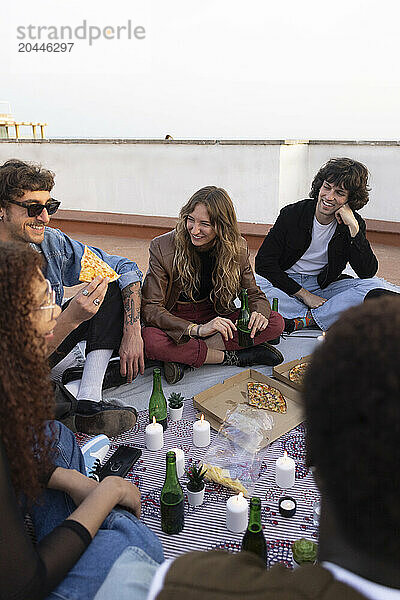 Happy male and female friends having pizza in party while sitting on rooftop