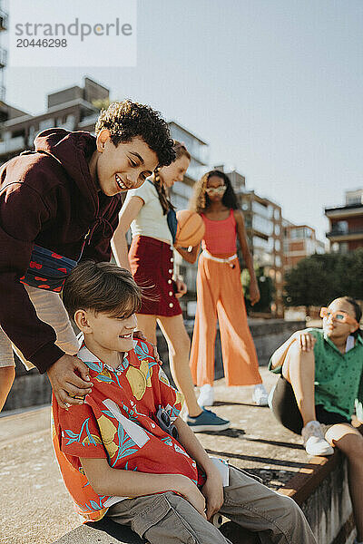 Playful boys with female friends siting on wall at street