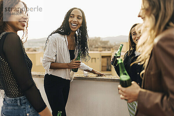 Carefree female friends holding beer bottles in party on building rooftop