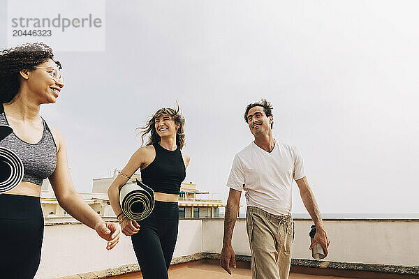 Happy male and female friends talking to each other while walking on building rooftop against sky