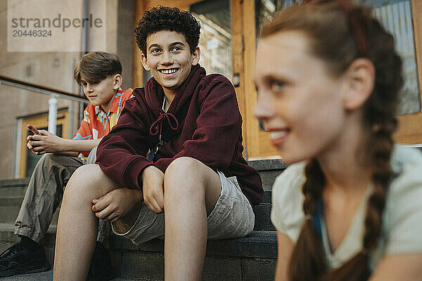 Smiling boy sitting with friends on staircase of school building entrance