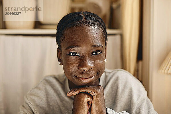 Portrait of smiling teenage boy with hands on chin at home