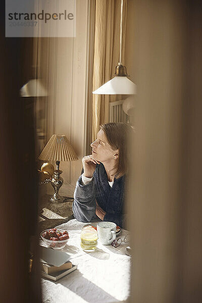 Senior woman sitting with hand on chin near dining table at home