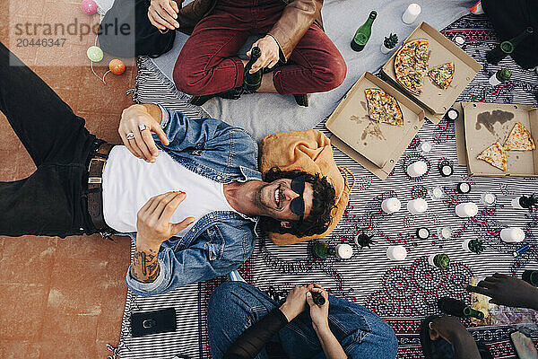 Directly above shot of happy man lying down on blanket by friends in party at rooftop