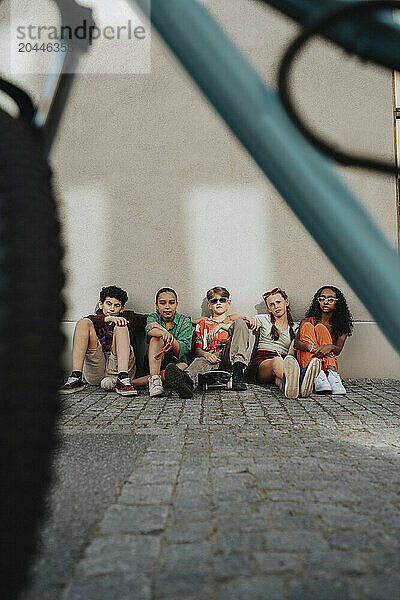 Fashionable boys and girls sitting on ground against wall