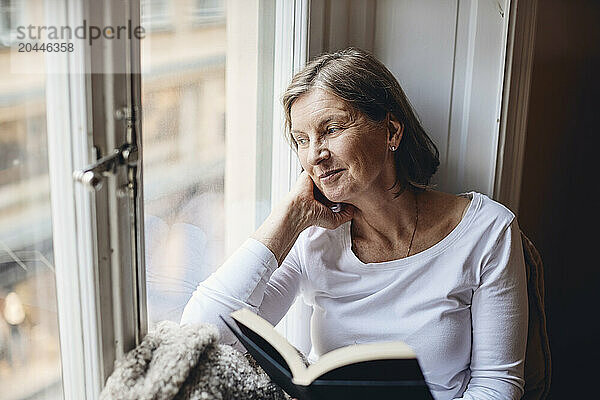 High angle view of smiling senior woman looking through window at home