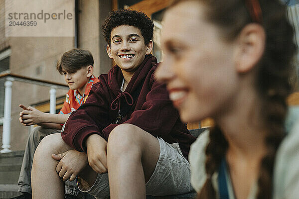 Portrait of smiling boy sitting with friends on staircase of school building entrance