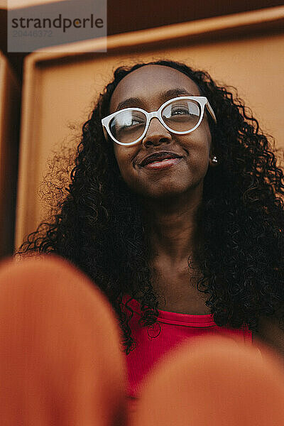 Smiling girl with curly hair and wearing eyeglasses looking away