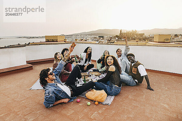 Cheerful male and female friends celebrating during party while sitting on rooftop