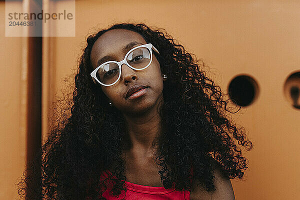 Portrait of teenage girl with curly hair wearing eyeglasses against metal structure