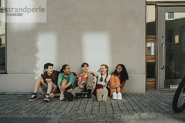 Happy boys and girls sitting on ground against wall