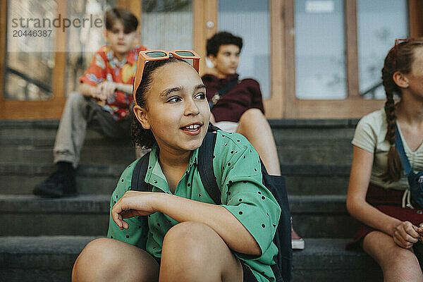 Girl wearing sunglasses sitting with friends on staircase of school building entrance