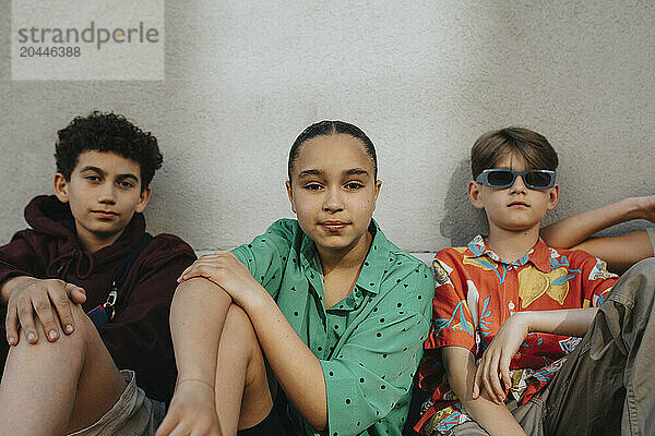 Portrait of girl sitting with boys against wall