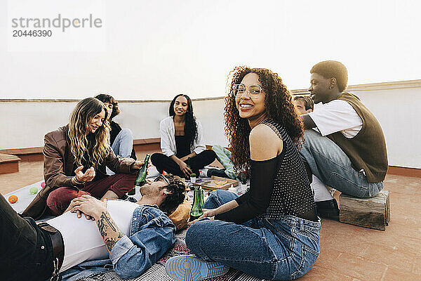 Side view portrait of smiling woman sitting with male and female friends during party on rooftop