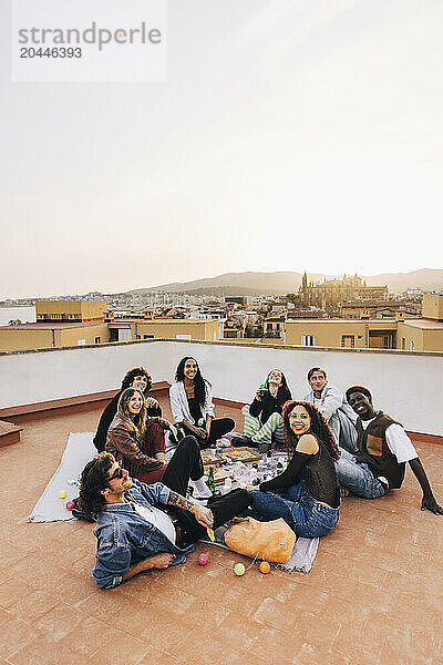 Group of multiracial male and female friends sitting on floor during party at rooftop