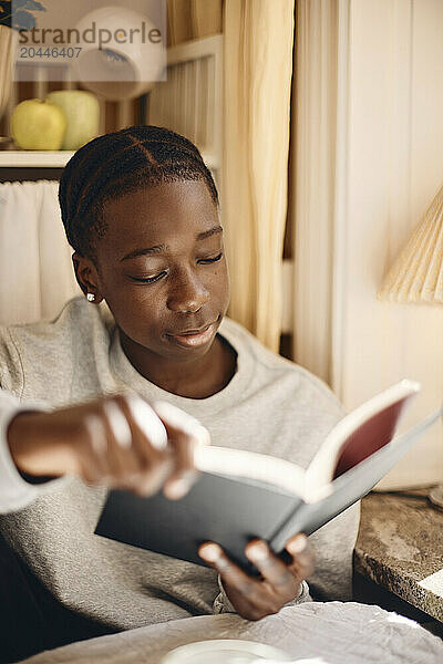 Teenage boy reading book while sitting at home