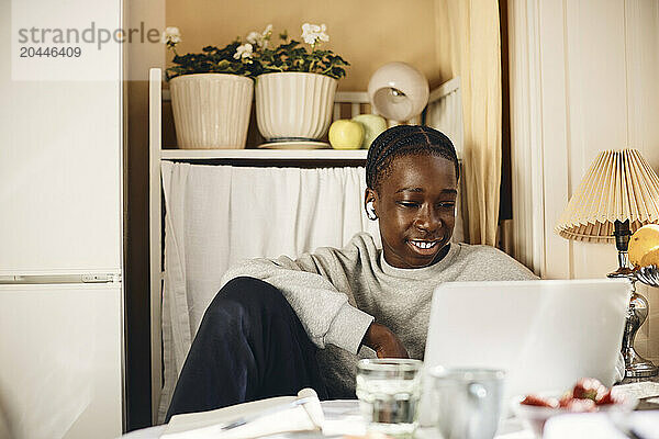 Smiling teenage boy using laptop while sitting at home