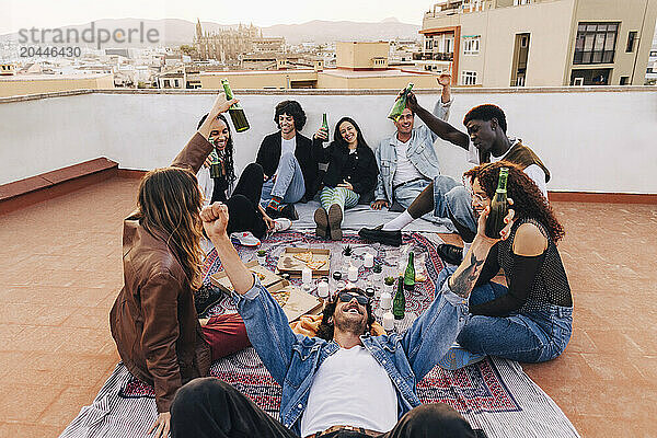 Carefree male and female friends toasting beer bottles during party celebration on rooftop