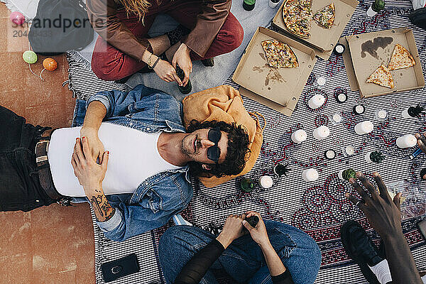 Directly above shot of man lying down by friends sitting on picnic blanket during party