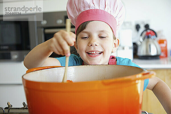 Smiling Girl Wearing Chef's Hat Stirring Casserole