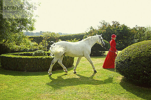 Woman in Red Equestrian Outfit Walking in Garden with Horse