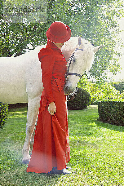 Woman in Red Equestrian Outfit Standing in Garden with Horse