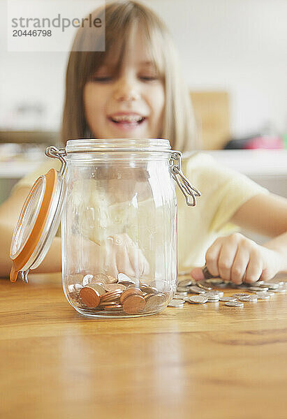 Smiling Young Girl Putting Coins in Jar