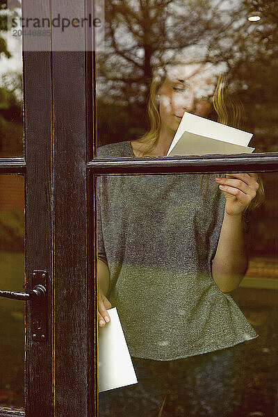 Young Woman Reading Letter behind Glass Door