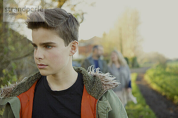 Teenage Boy Walking in Country Road  Parents in Background